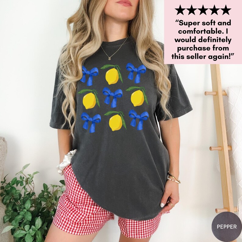 K&ouml;nnte beinhalten: Ein dunkelgraues T-Shirt mit einem Zitronen- und blauen Schleifenmuster. Das Shirt ist Oversize und hat eine lockere Passform.