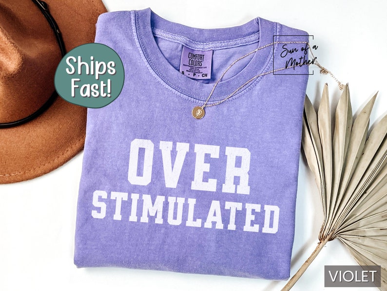 May include: A purple t-shirt with the text "OVER STIMULATED" in white. The shirt is made of a soft, comfortable material and is perfect for everyday wear.