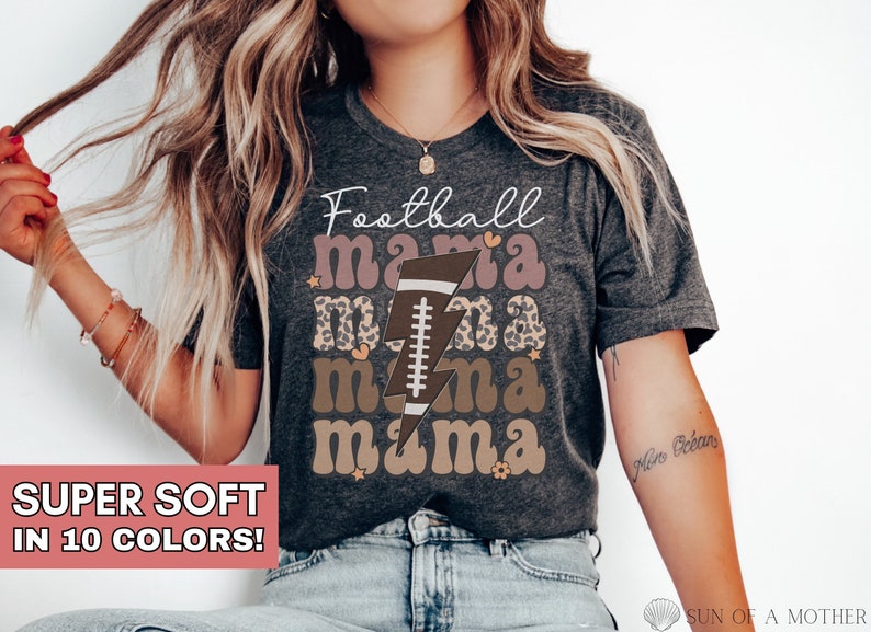 Puede incluir: Una camiseta gris con el texto "Football mama mama mama" en letras marrones y rosas con un rayo y un gr&aacute;fico de f&uacute;tbol.