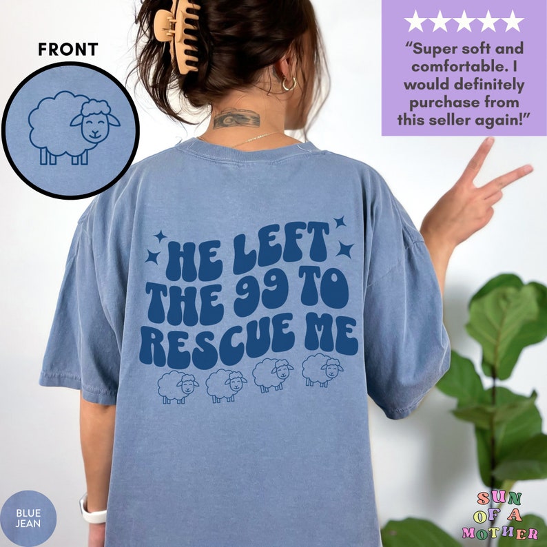 May include: A light blue t-shirt with a graphic print of the text "He left the 99 to rescue me" in a retro font. The graphic also includes four cartoon sheep. The shirt is shown on a model.