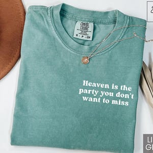 May include: Light green t-shirt with the text "Heaven is the party you don't want to miss" printed in white. The shirt is made of a soft, comfortable material and has a distressed look.