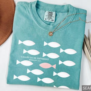 May include: A teal blue t-shirt with a white fish pattern and the text "Called to be different Romans 12:2".