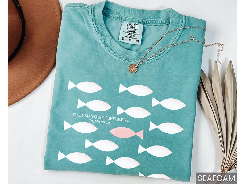 May include: A teal blue t-shirt with a white fish pattern and the text "Called to be different Romans 12:2".