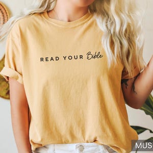 May include: A mustard yellow t-shirt with the text "READ YOUR Bible" printed in black.