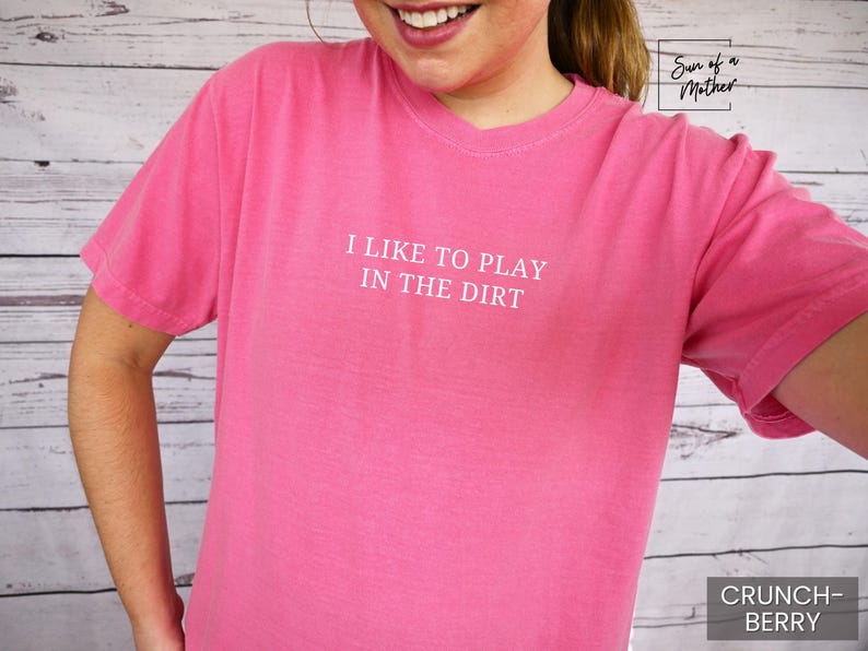 May include: Pink t-shirt with the text "I like to play in the dirt" printed in white.