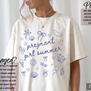 May include: Ivory-colored t-shirt with blue summer-themed graphics and the text "pregnant girl summer." The design includes a palm tree, seashells, bows, and a watermelon slice. The shirt is a relaxed fit.