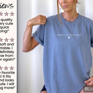 Puede incluir: Una camiseta azul vaquero con la frase "reading is my favorite sport" y un peque&ntilde;o coraz&oacute;n blanco. La camiseta es de manga corta y cuello redondo.