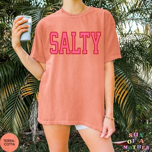 May include: A coral colored oversized t-shirt with the word "SALTY" printed in bold pink letters.