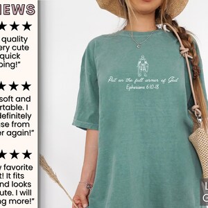 Puede incluir: Una camiseta verde claro con el texto "Put on the full armor of God Ephesians 6:10-18" en blanco. La camiseta presenta un peque&ntilde;o gr&aacute;fico de una persona con armadura.