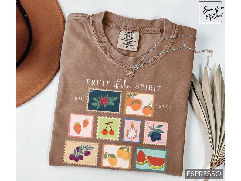 May include: A brown t-shirt with the text "FRUIT of the SPIRIT" and a graphic of nine postage stamps featuring different fruits. The stamps are labeled with the text "GAL" and "5:22-23".