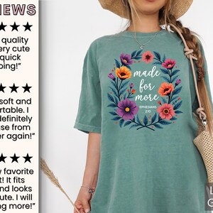 K&ouml;nnte beinhalten: Ein hellgr&uuml;nes T-Shirt mit einem floralen Kranz-Design und dem Text "made for more" mit dem Bibelvers "Epheser 2:10".