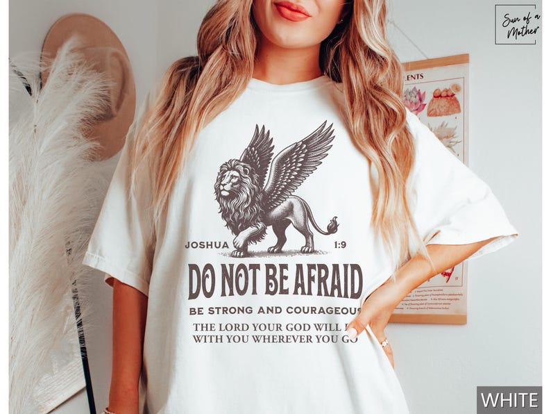 May include: White t-shirt featuring a detailed illustration of a winged lion with the text "DO NOT BE AFRAID" and a Bible verse. The shirt's design includes the word "Joshua" and the number "1:9".