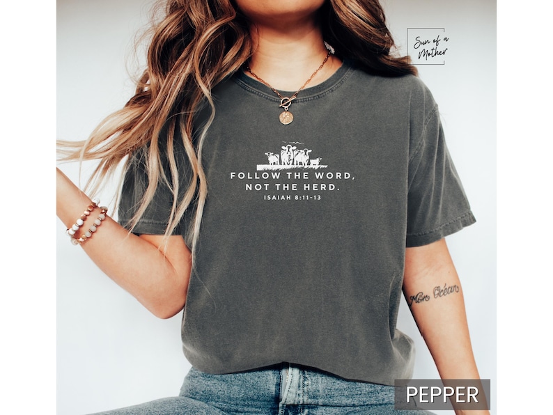 Peut inclure: Un t-shirt gris fonc&eacute; avec un motif blanc repr&eacute;sentant un groupe de moutons et le texte "FOLLOW THE WORD, NOT THE HERD. ISAIAH 8:11-13".