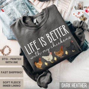 May include: Dark heather grey sweatshirt with the text "Life is better with my chickens" printed in white. The sweatshirt features a graphic of five chickens, including a black and white chicken, a brown chicken, a white chicken, and two yellow chicks.