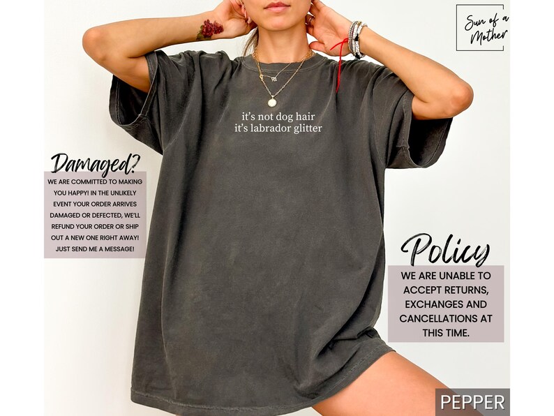 May include: Dark gray t-shirt with the text "it's not dog hair it's labrador glitter" in white. The shirt has a relaxed fit. Additional text on the image includes "Damaged?" and "Policy".