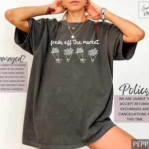 May include: Dark grey t-shirt with the text "fresh off the market" and four bouquets of flowers. The shirt has a relaxed fit and is made of a soft material. The shirt is a casual wear item.