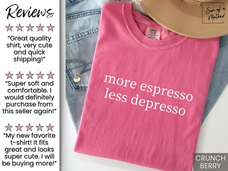 Op de afbeelding: Een Crunch Berry gekleurd t-shirt met de witte tekst "more espresso less depresso". Het shirt is opgevouwen en op een spijkerbroek gelegd. Een beige hoed is zichtbaar op de achtergrond.