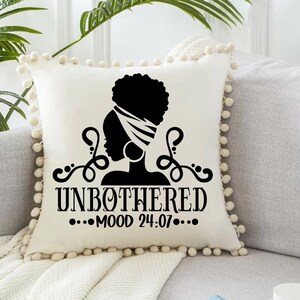 May include: White throw pillow with a black silhouette of a woman with a head wrap and the text "UNBOTHERED...MOOD 24:07..."