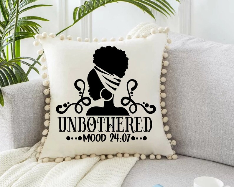 May include: White throw pillow with a black silhouette of a woman with a head wrap and the text "UNBOTHERED...MOOD 24:07..."