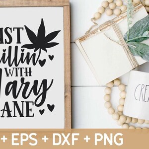 May include: A white wooden sign with black text that reads "Just chillin' with Mary Jane" and a black marijuana leaf graphic. The sign is surrounded by a wooden frame.