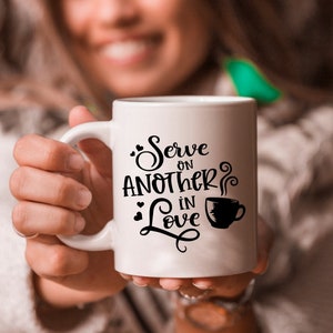 Puede incluir: Taza de cer&aacute;mica blanca con texto negro que dice "Serve on another in love" con un peque&ntilde;o gr&aacute;fico de taza de caf&eacute; negro.
