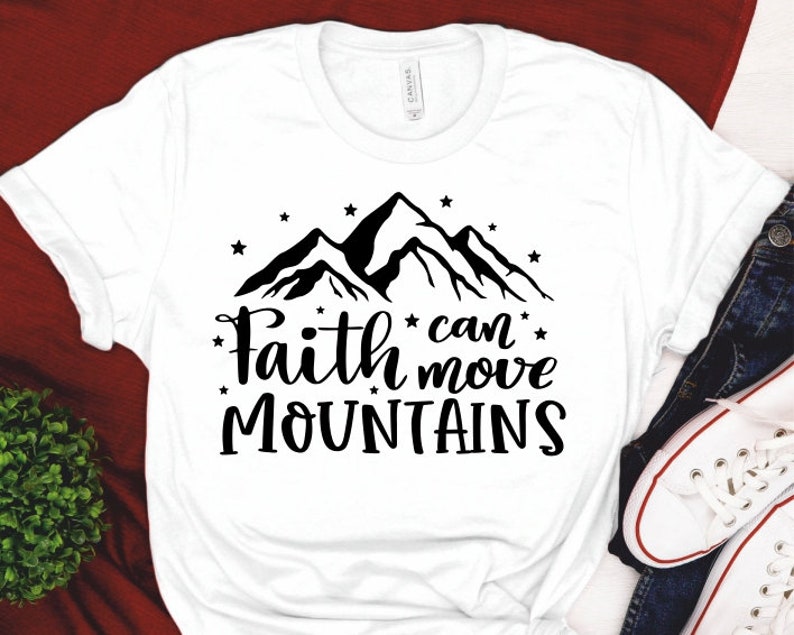 Puede incluir: Camiseta blanca con un gr&aacute;fico de una cadena monta&ntilde;osa negra y el texto "Faith can move mountains".