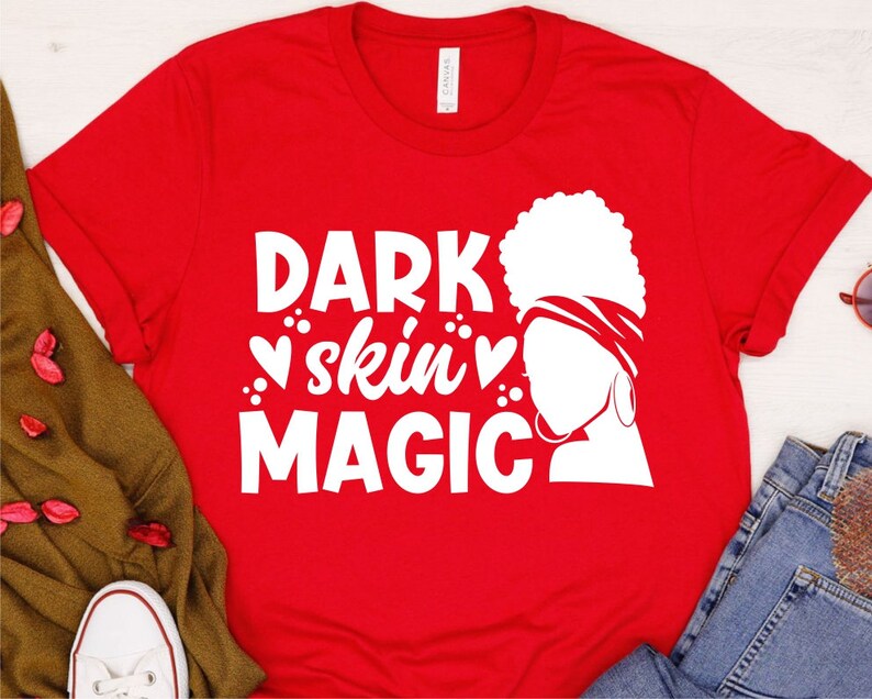 May include: Red t-shirt with a white graphic design featuring a woman's silhouette with a headscarf and the text "DARK skin MAGIC" with hearts.