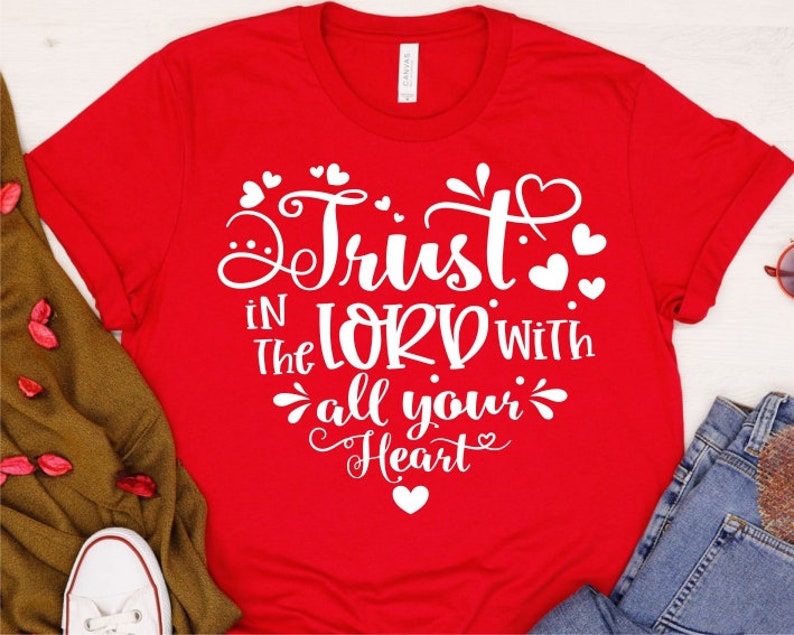 Puede incluir: Camiseta roja con texto blanco que dice "Trust in the Lord with all your heart" rodeado de peque&ntilde;os corazones.