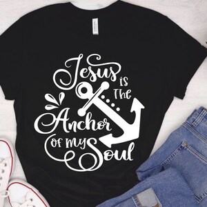 Puede incluir: Camiseta negra con un dise&ntilde;o gr&aacute;fico blanco que dice "Jes&uacute;s es el ancla de mi alma" con un gr&aacute;fico de ancla.