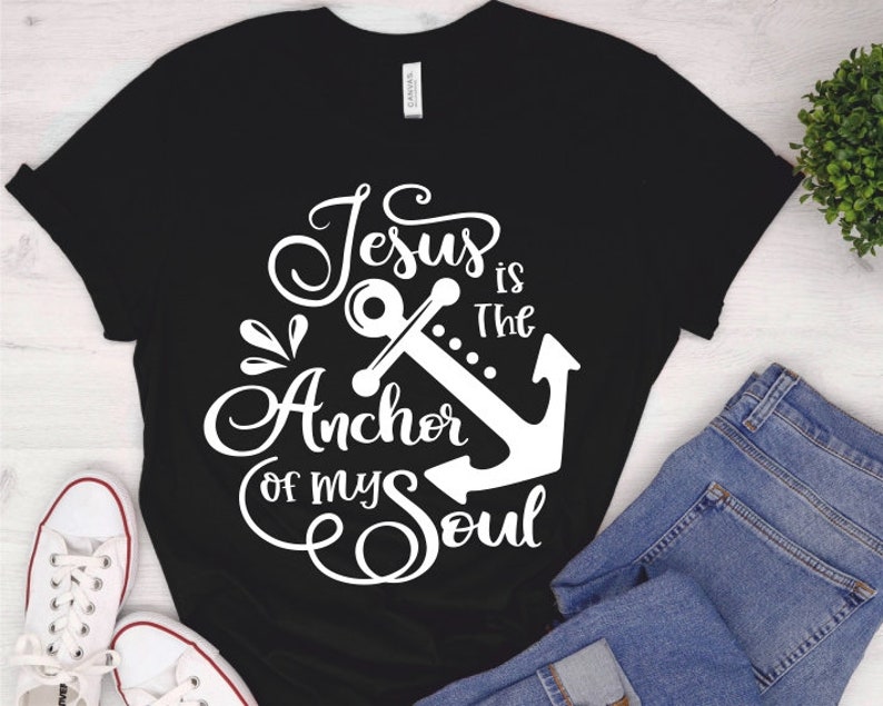 Puede incluir: Camiseta negra con un dise&ntilde;o gr&aacute;fico blanco que dice "Jes&uacute;s es el ancla de mi alma" con un gr&aacute;fico de ancla.