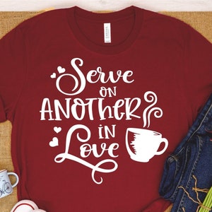 Puede incluir: Camiseta roja con texto blanco que dice "Serve on another in love" con un gr&aacute;fico de taza de caf&eacute; estilizado.