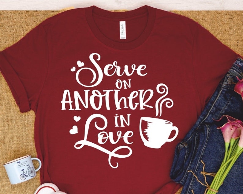 Puede incluir: Camiseta roja con texto blanco que dice "Serve on another in love" con un gr&aacute;fico de taza de caf&eacute; estilizado.