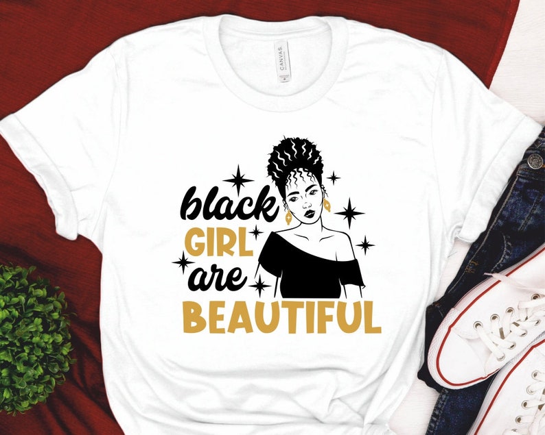 May include: White t-shirt with a black silhouette of a woman with a gold crown and the text "black girl are beautiful" in gold letters.