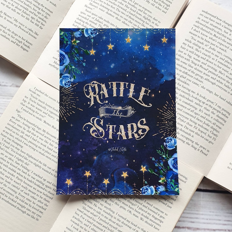 May include: A book cover with a blue watercolor background featuring stars and blue flowers. The title "Rattle the Stars" is written in gold glitter lettering.
