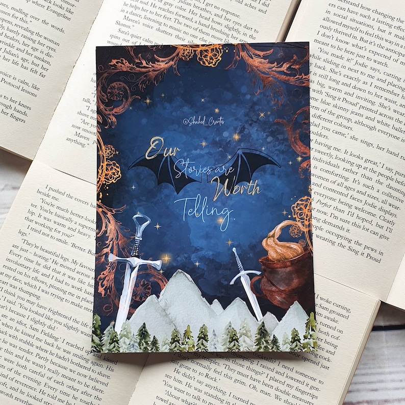 以下が含まれることがあります： 星、山、木のある濃い青色の空の水彩画。2本の剣が山脈の前に交差している。蓋のある大釜が画像の右側にある。「私たちの物語は語る価値がある。」というテキストが画像の中央にある。