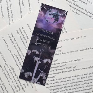 May include: A black and purple bookmark with a wolf's head and two swords. The bookmark has the text "There's a grain of truth in every fairy tale".
