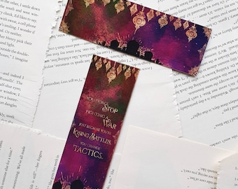 May include: Two bookmarks with a watercolour background featuring a silhouette of people and hanging lanterns. The text on the bookmark reads "You don't stop fighting a war just because you're losing battles. You change tactics."