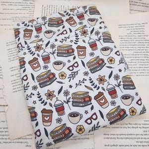 May include: A light blue fabric with a repeating pattern of books, coffee cups, coffee to-go cups, eyeglasses, flowers, and leaves. The design features brown, orange, and white elements. The fabric is folded and appears to be a pouch or bag.