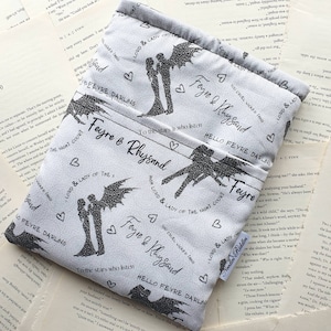 Könnte beinhalten: Eine weiße Stoffbuchhülle mit einem sich wiederholenden Muster in Schwarzweiß von einem Paar mit Flügeln. Der Text "Feyre & Rhysand" wird im gesamten Muster wiederholt. Der Text "High Lord & Lady of the Night Court" wird ebenfalls im gesamten Muster wiederholt. Der Text "You cruel wicked thing" wird im gesamten Muster wiederholt. Der Text "To the stars who listen" wird im gesamten Muster wiederholt. Der Text "Hello Feyre Darling" wird im gesamten Muster wiederholt.