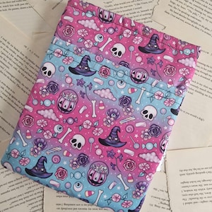 May include: A pink and blue drawstring bag with a Halloween-themed print. The print features skulls, pumpkins, candy, stars, and witch hats. The bag is ideal for carrying small items like sweets or trinkets.