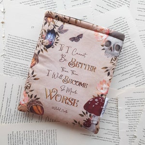 May include: A beige book sleeve with a floral design and a skull. The text on the sleeve reads "If I Cannot Be Better Than Then, I Will Become So Much Worse" with the hashtag "#ShakedCrafts".