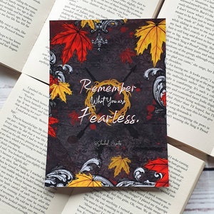 May include: A motivational quote card with a dark grey background and a wreath of autumn leaves in shades of red, orange, and yellow. The quote reads "Remember What You Are Fearless."