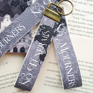 May include: Two grey fabric bookmarks with the text "No Funerals" and "No Mourners" printed in white. The bookmarks are attached to a gold-coloured key ring.
