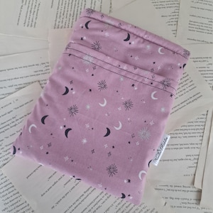 Könnte beinhalten: Ein lavendelfarbener Stoffbeutel mit einem Himmelsmuster aus Monden, Sternen und Sonnenstrahlen. Das Design umfasst schwarze, weiße und silberne Akzente. Der Beutel ist rechteckig mit einer Tasche und einem kleinen Etikett mit der Aufschrift "Noodle Riddles".