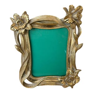 May include: A gold-toned picture frame with a green background and floral accents. The frame is ornate and features a stylised floral design.