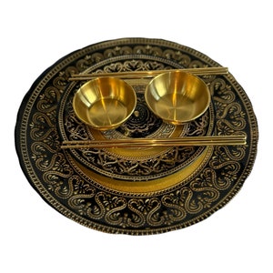 Puede incluir: Un plato redondo negro y dorado con diseños intrincados, que incluye dos cuencos dorados y un par de palillos dorados.