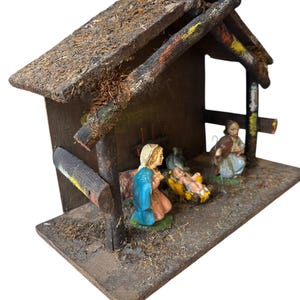 Pode incluir: Um pres&eacute;pio r&uacute;stico de madeira com telhado de palha. A cena inclui figuras de Maria com uma t&uacute;nica azul, Jos&eacute; e o menino Jesus numa manjedoura. As figuras s&atilde;o pintadas com cores vivas. Uma decora&ccedil;&atilde;o de Natal tradicional.
