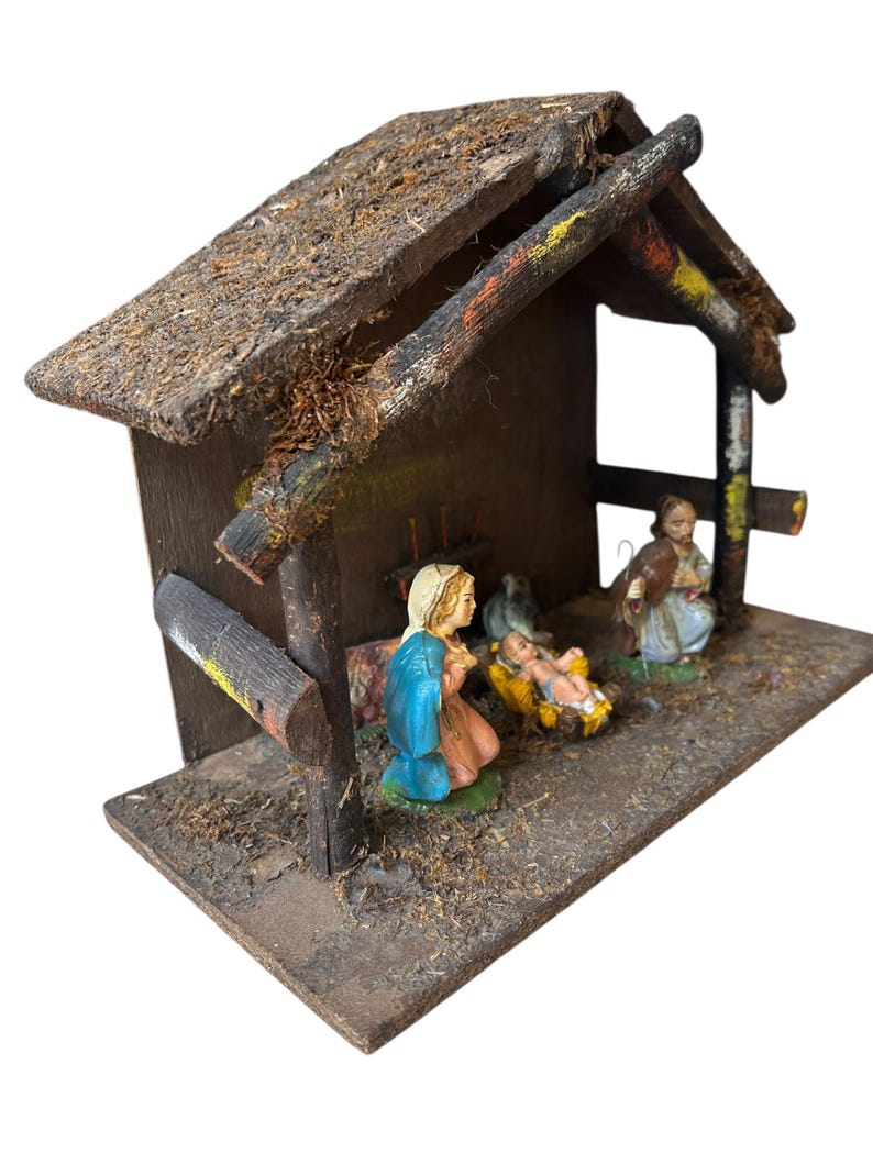 Pode incluir: Um pres&eacute;pio r&uacute;stico de madeira com telhado de palha. A cena inclui figuras de Maria com uma t&uacute;nica azul, Jos&eacute; e o menino Jesus numa manjedoura. As figuras s&atilde;o pintadas com cores vivas. Uma decora&ccedil;&atilde;o de Natal tradicional.
