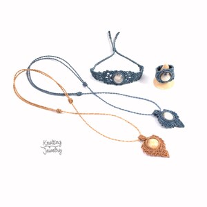 Op de afbeelding: Een set van drie macramé sieraden met blauwe en bruine koorden. De set bevat een armband, een ring en een ketting met een hanger. De hanger en de ring hebben een ronde, witte steen.