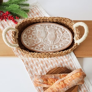 May include: An oval ceramic tray featuring a relief design of two owls perched on a branch surrounded by stars, nestled inside a woven seagrass basket with two thick rope handles. The tray has a light brown finish with white detailing.